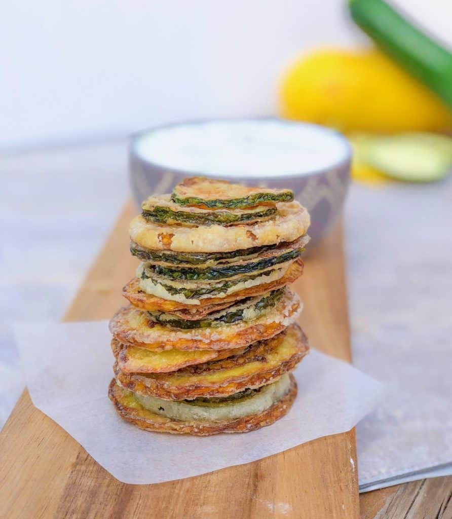 Homemade crispy zucchini chips in a tall tower on cutting board.