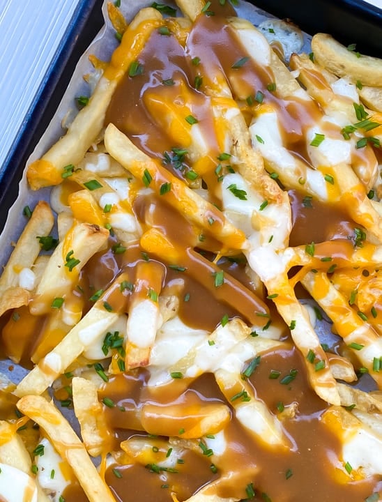 gravy fries finger food smothered in cheese on a baking sheet.