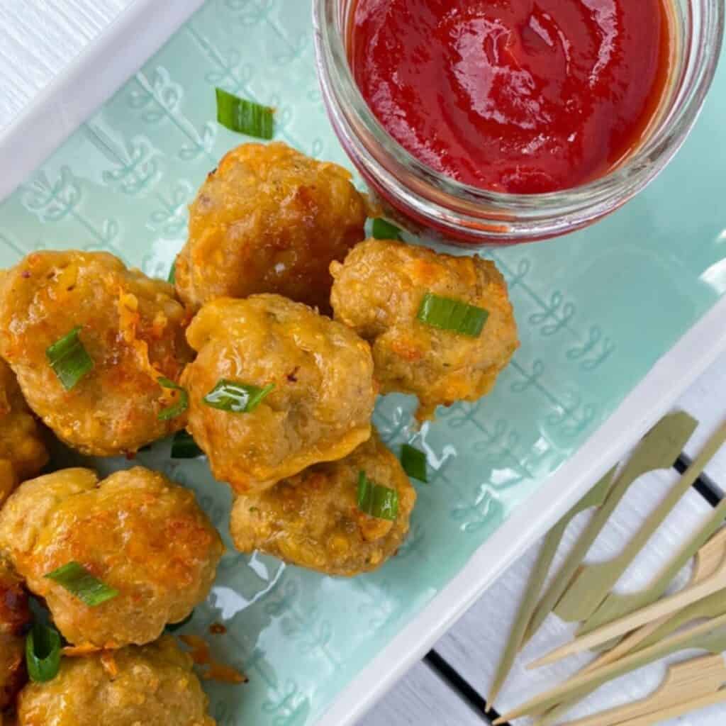 sausage balls appetizer on a plate with toothpick skewers and dipping sauce.