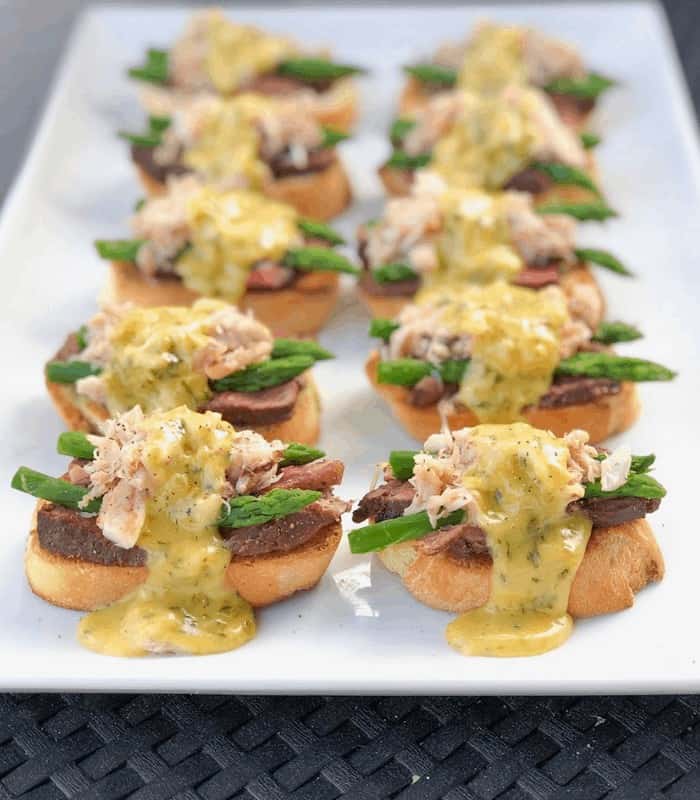 crostini with steak, crab, asparagus and sauce on plate.