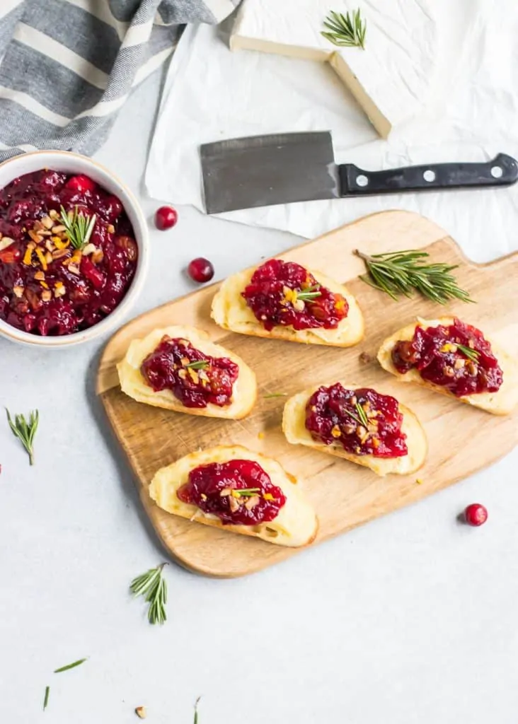 brie crostini with cranberry chutney on a cutting board with knife on side.
