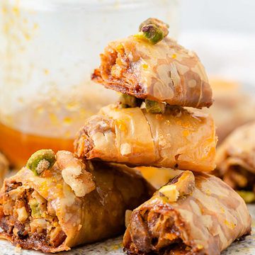 Baklava rolls stacked on table with honey.