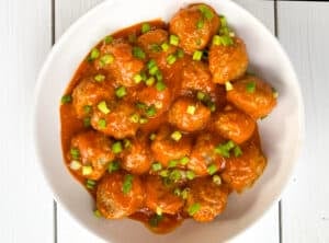 buffalo chicken meatballs in a white bowl topped with scallions