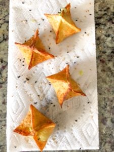 Draining avocado cream cheese wontons with sesame.