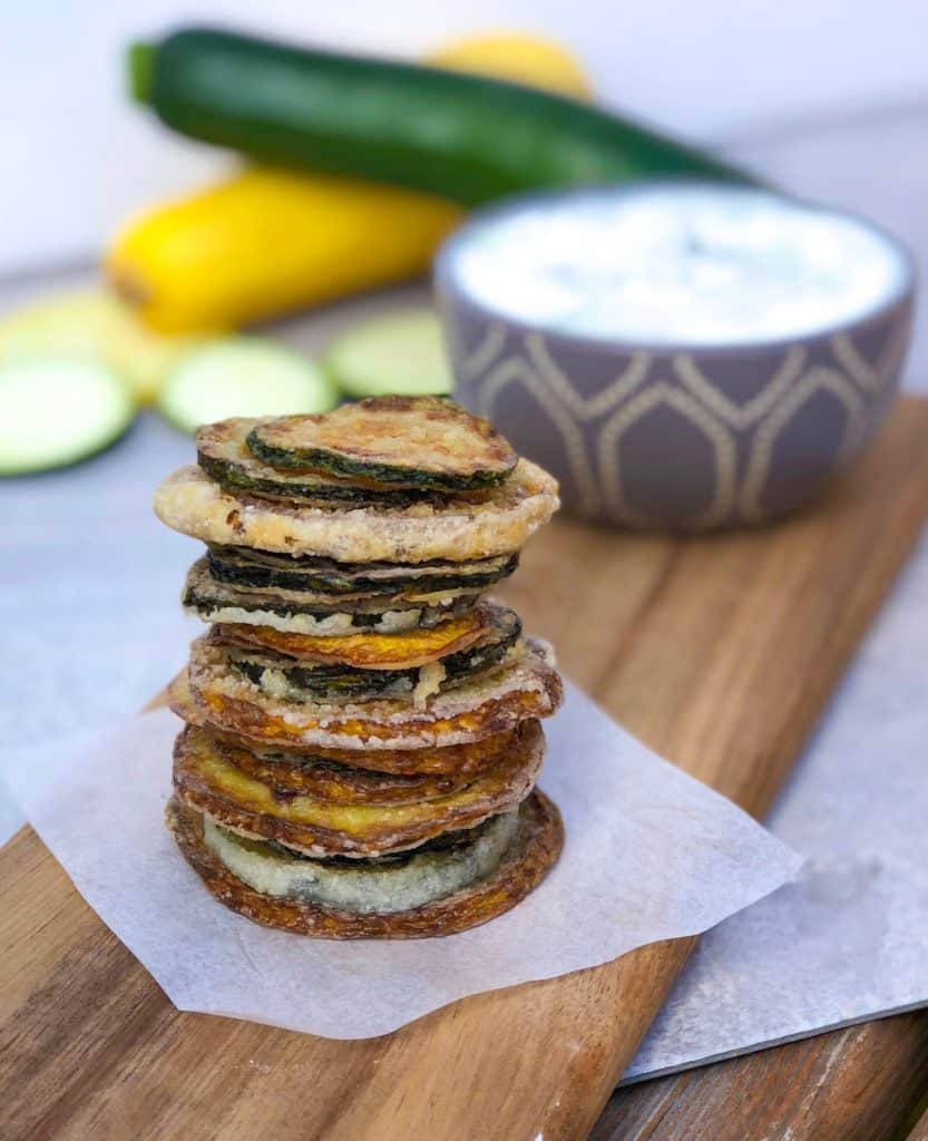 fried zucchini chips stacked on a cutting board