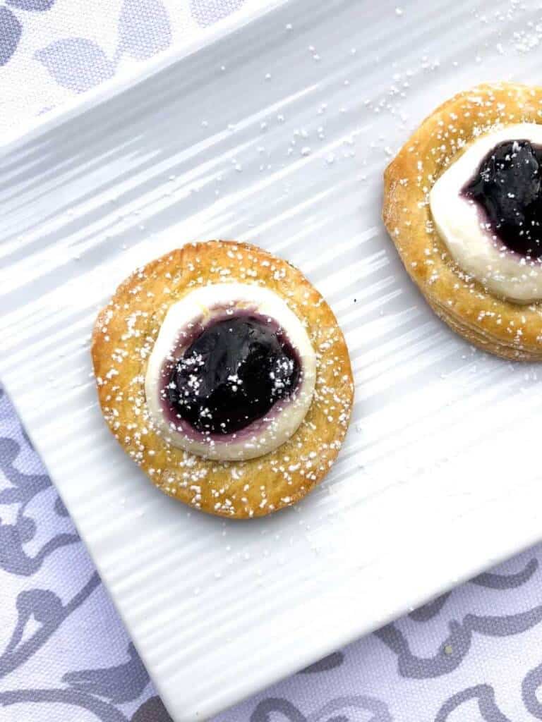 mini crescent dough rounds topped with a sweet cheese and blueberry pie filling on a white plate