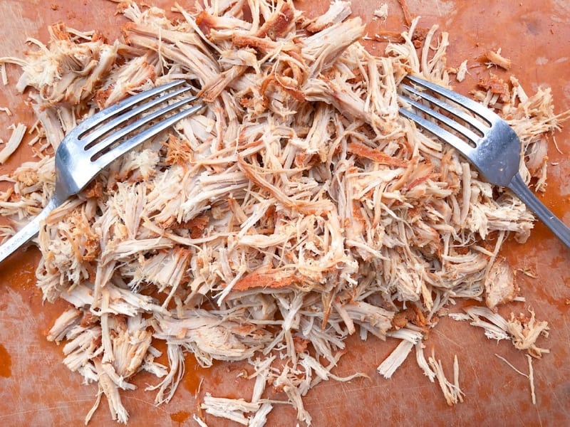 pulling pork on a cutting board using two forks