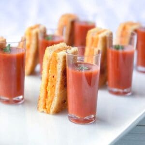 Grilled cheese sticks with tomato soup shooters on a plate.