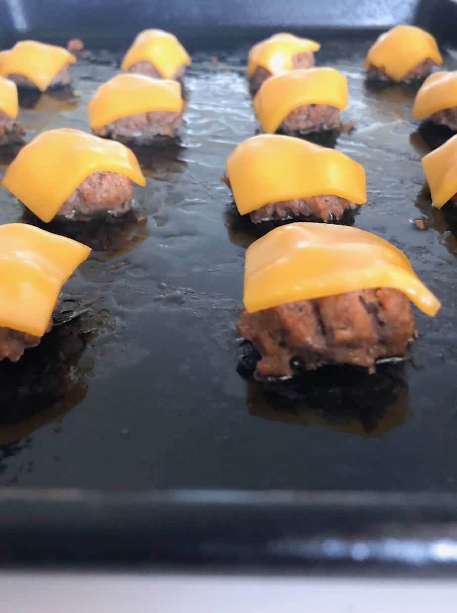 Mini cheeseburger patties on baking sheet.