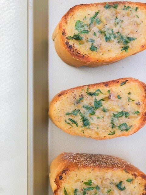 Garlic bread on a baking sheet with parsley.
