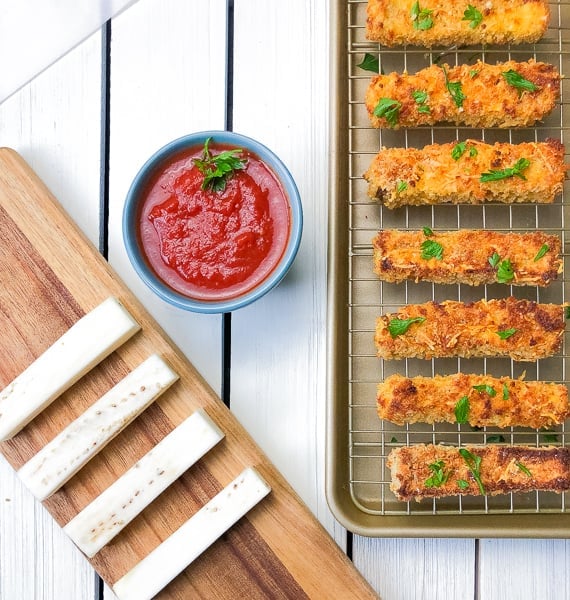 Eggplant french fries on a cutting board and baking sheet.