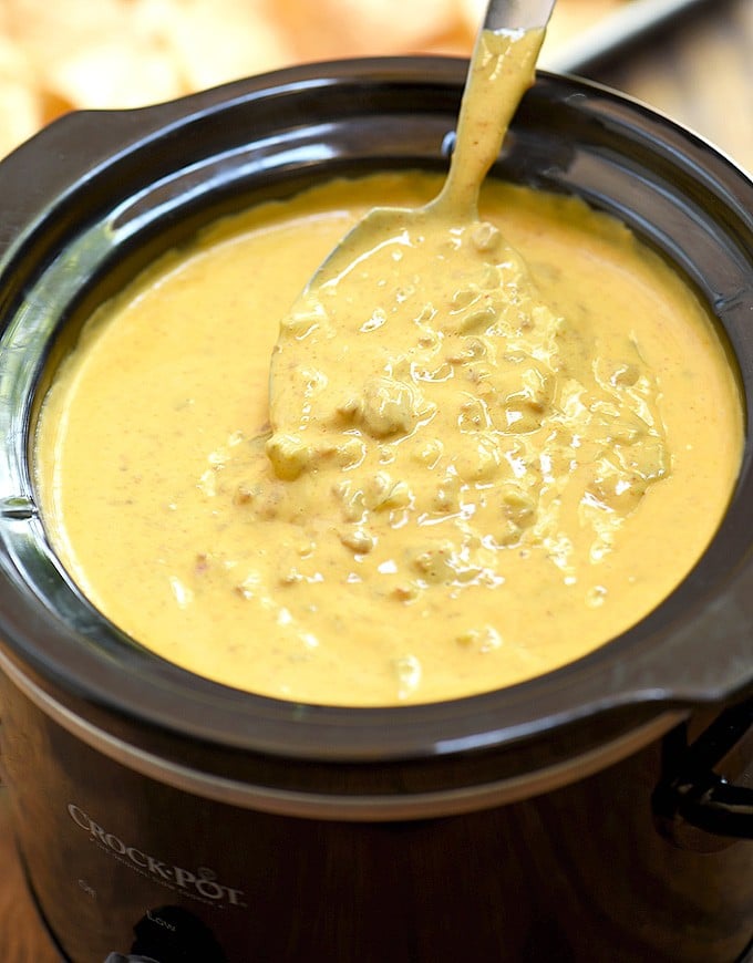 melted queso cheese with beer inside of a slow cooker with a spoon.