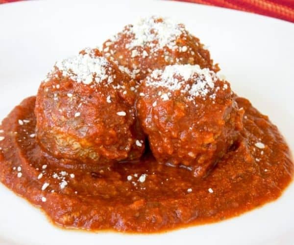 Three meatballs on a plate topped with Parmesan cheese.