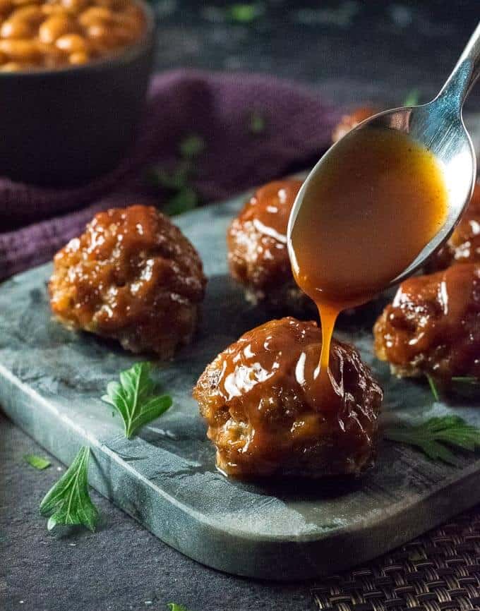 Meatballs being topped with BBQ sauce.