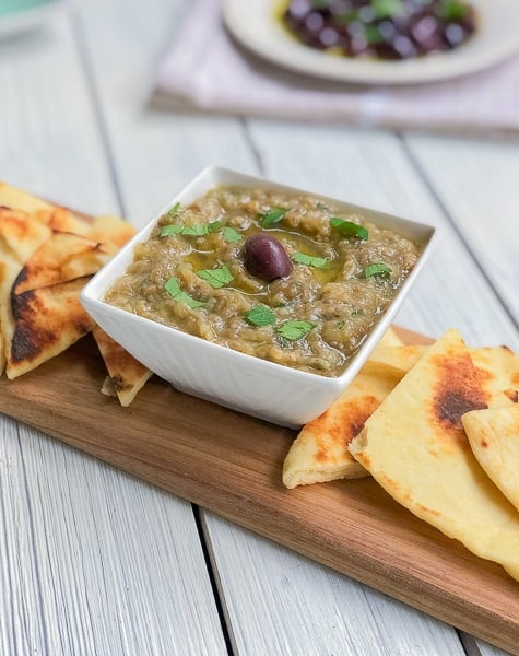 eggplant dip in a white bowl on cutting board with pita triangles