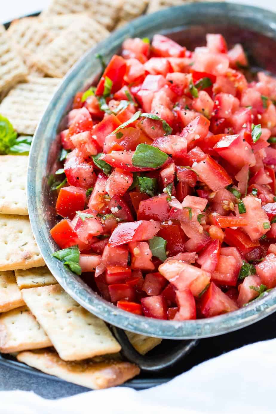 Chopped tomatoes with basil in a bowl with crackers on the side.