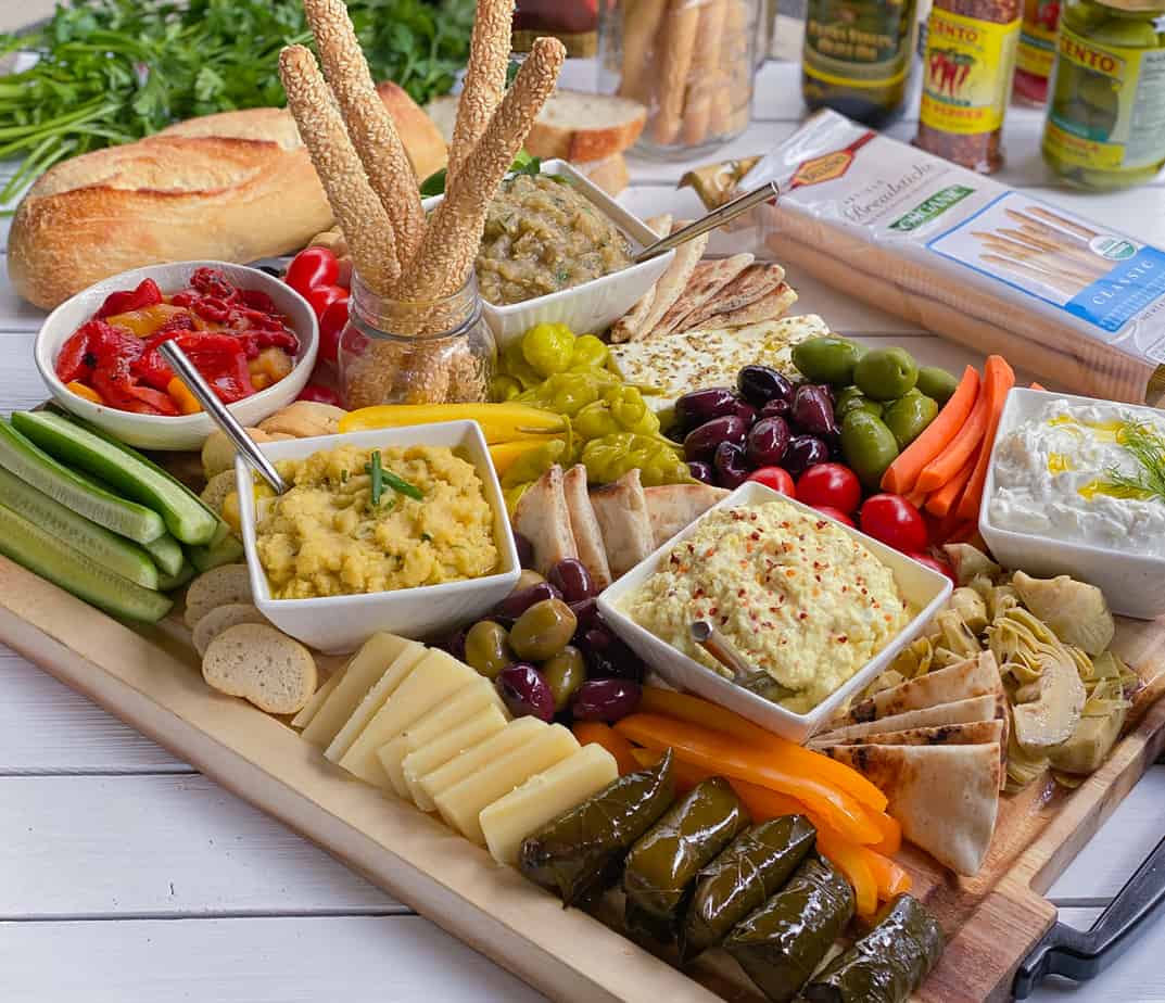 Large Greek appetizer platter with dolmades, pita bread, dips, veggies and olives.