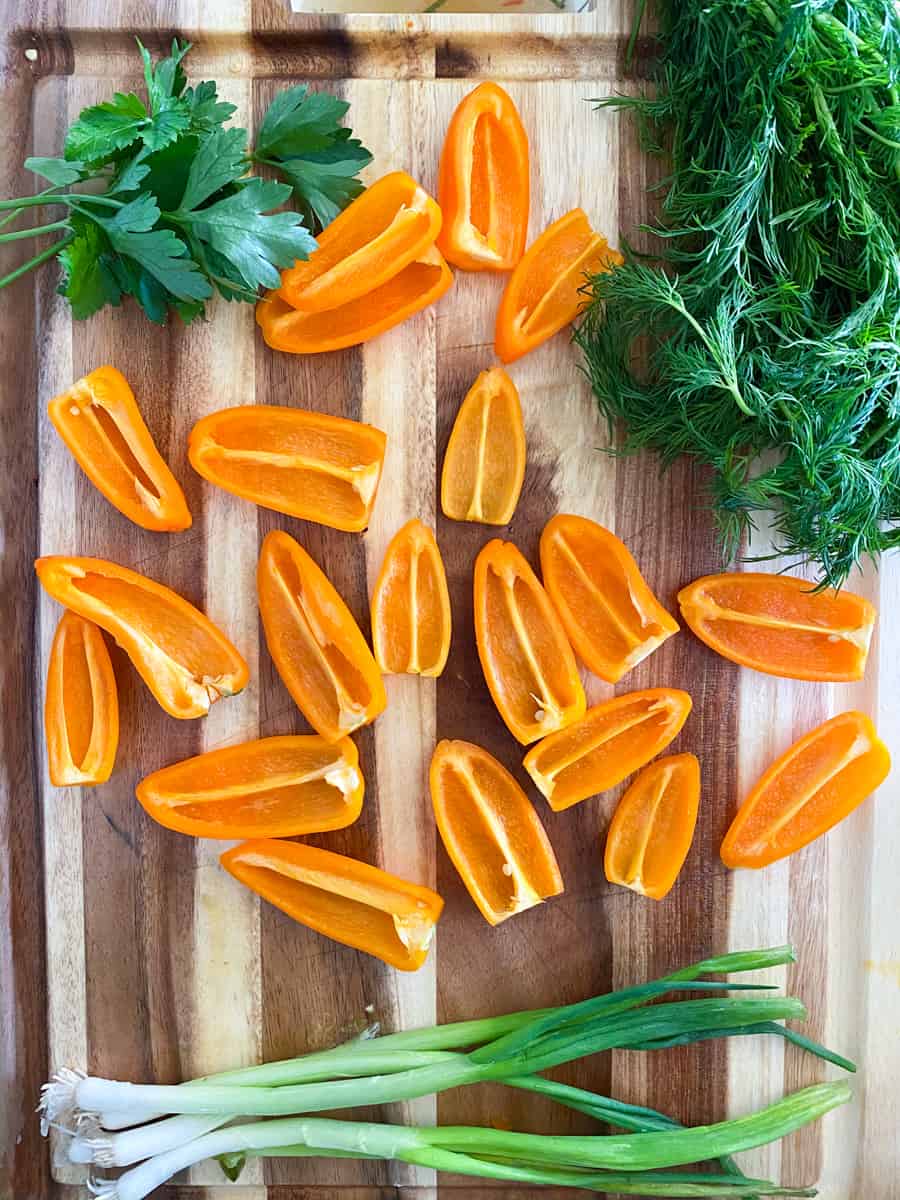 orange peppers dill leaves and chives on a cutting board.