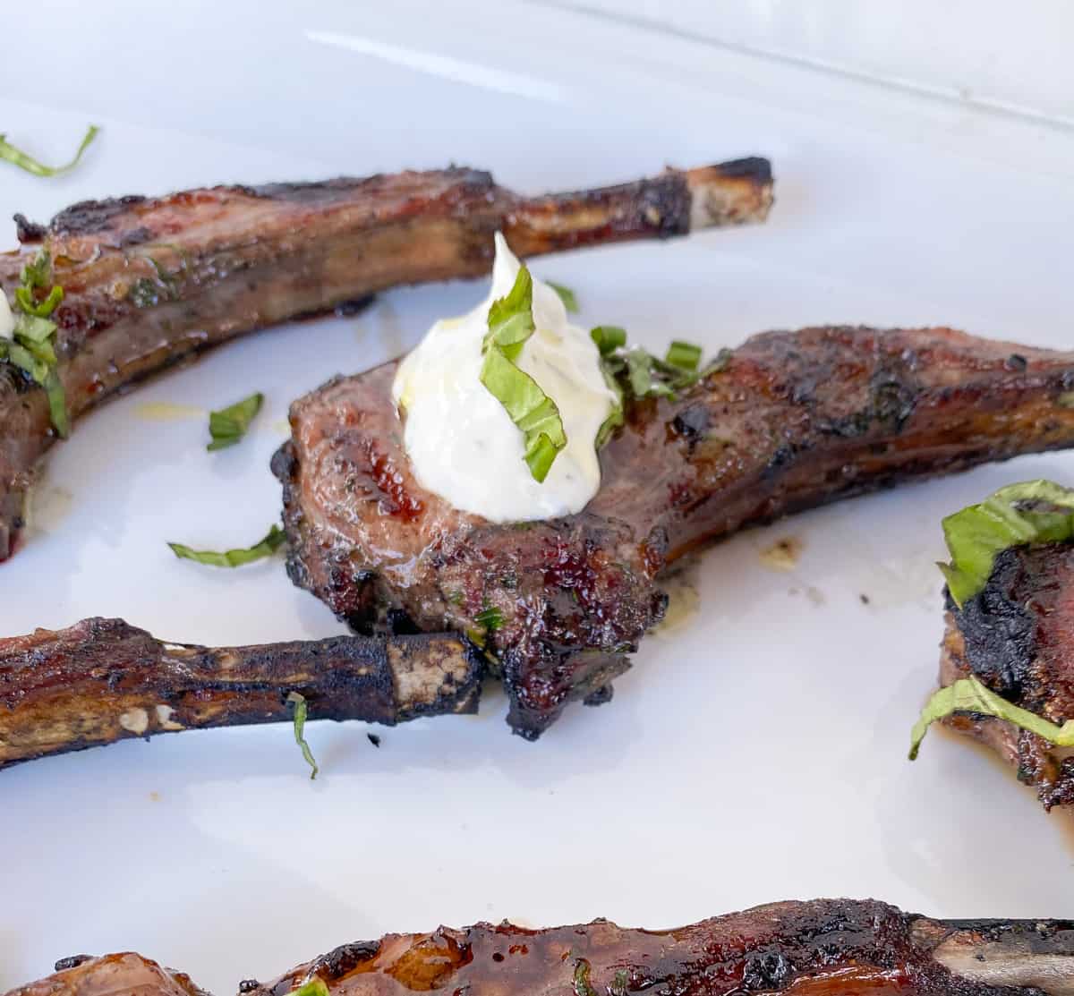 Grilled lamb lollipops on a plate with tzatziki sauce and mint.