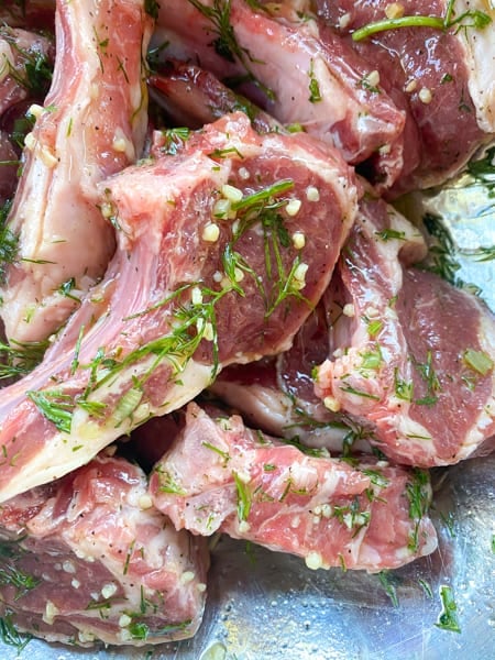 Lamb lollipops marinating in garlic herb oil before grilling.