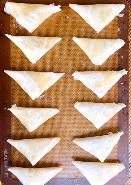 folded spanakopita triangles on a baking sheet.