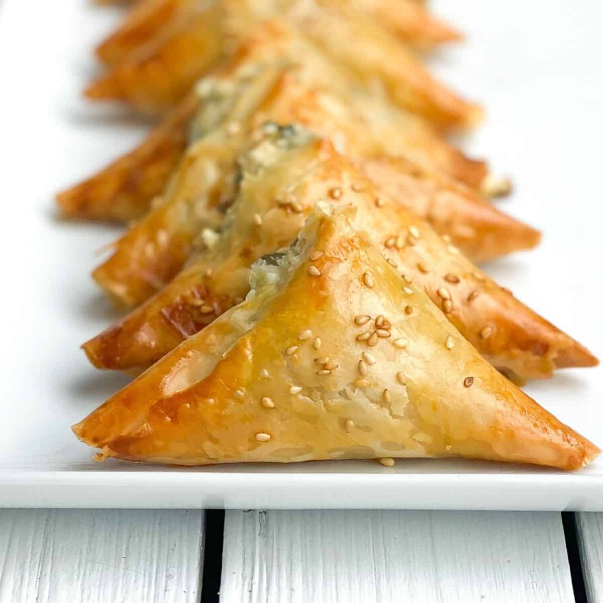 mini spanakopita pies on a white plate lined up.