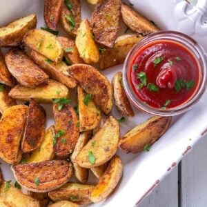 Crispy oven baked potato wedges in a white dish with ketchup.