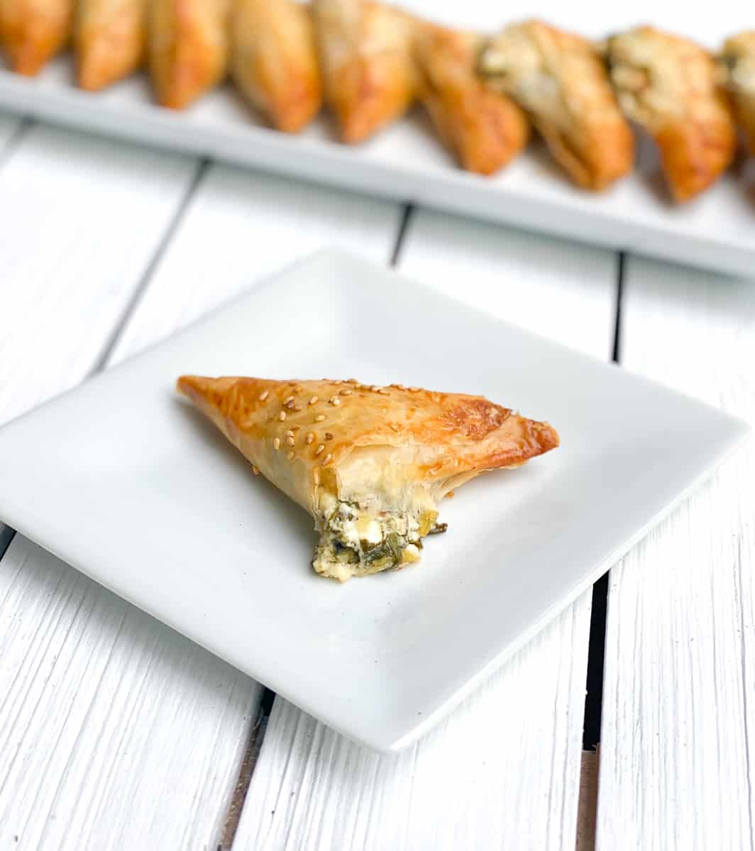 Mini spinach pies with feta cheese filling spilling out.