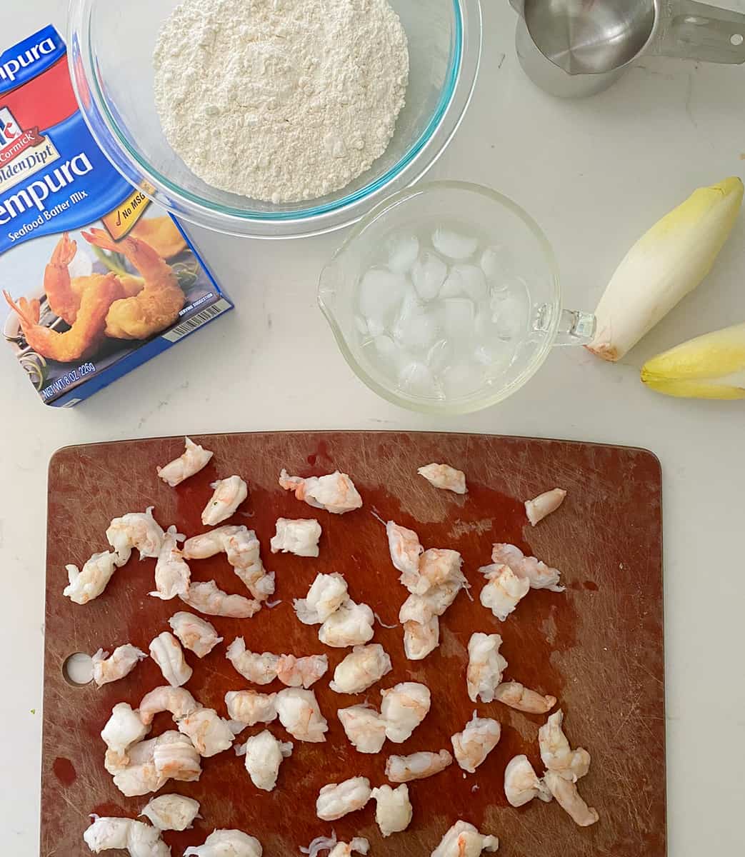 Chopped shrimp on a cutting board with endive leaves and ice water.