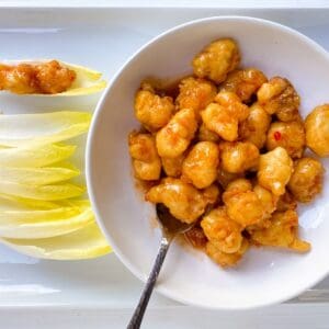 shrimp tempura with chili sauce in a white bowl with a spoon and endive leaves on the side