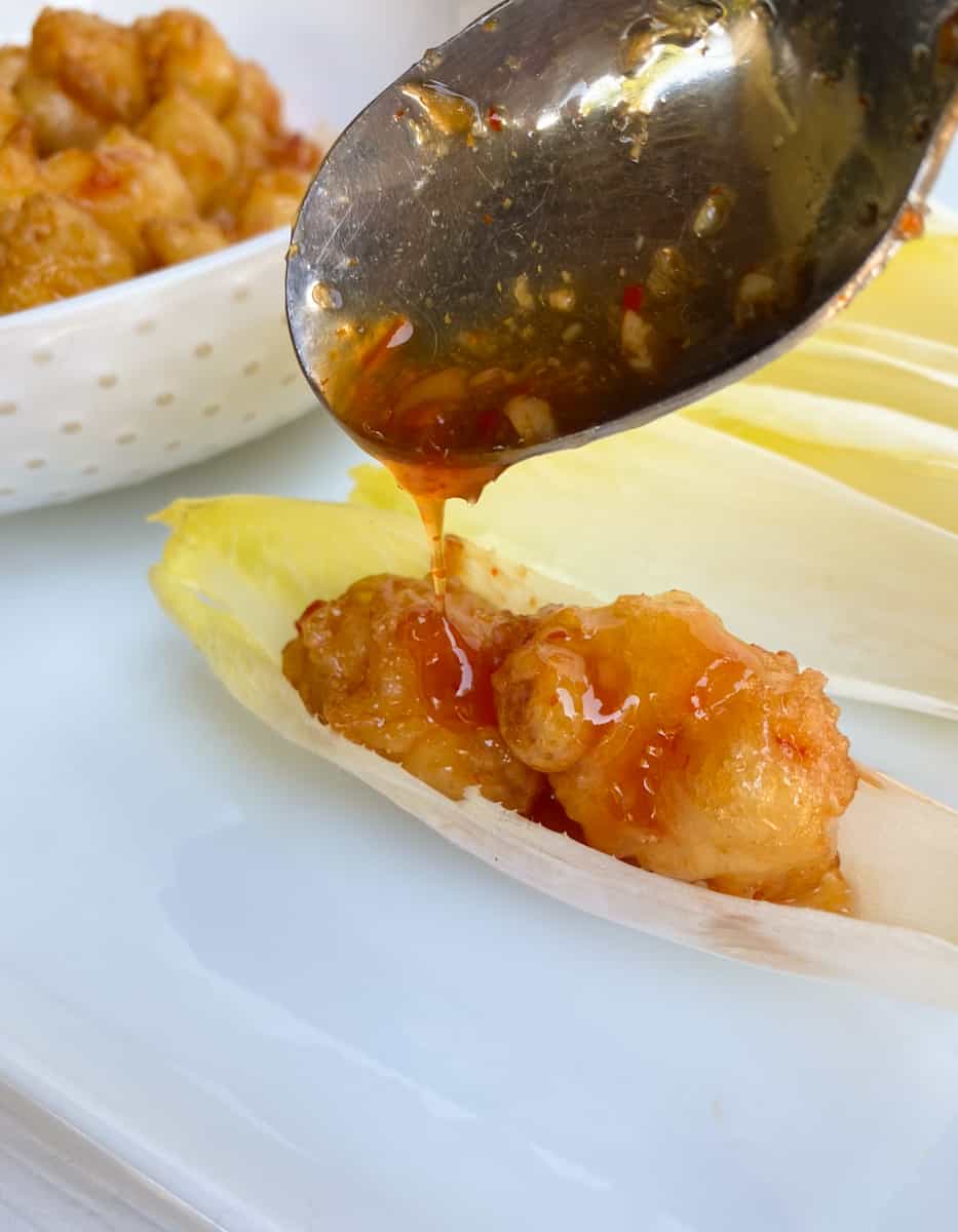 Shrimp tempura appetizer inside an endive leaf with chili sauce poured over top.