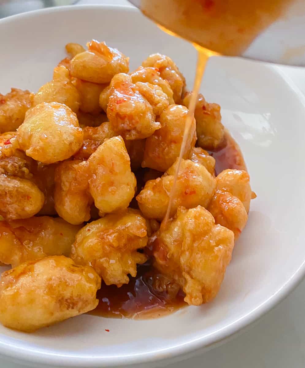 Shot of bowl pouring chili sauce over top of fried shrimp in a bowl.