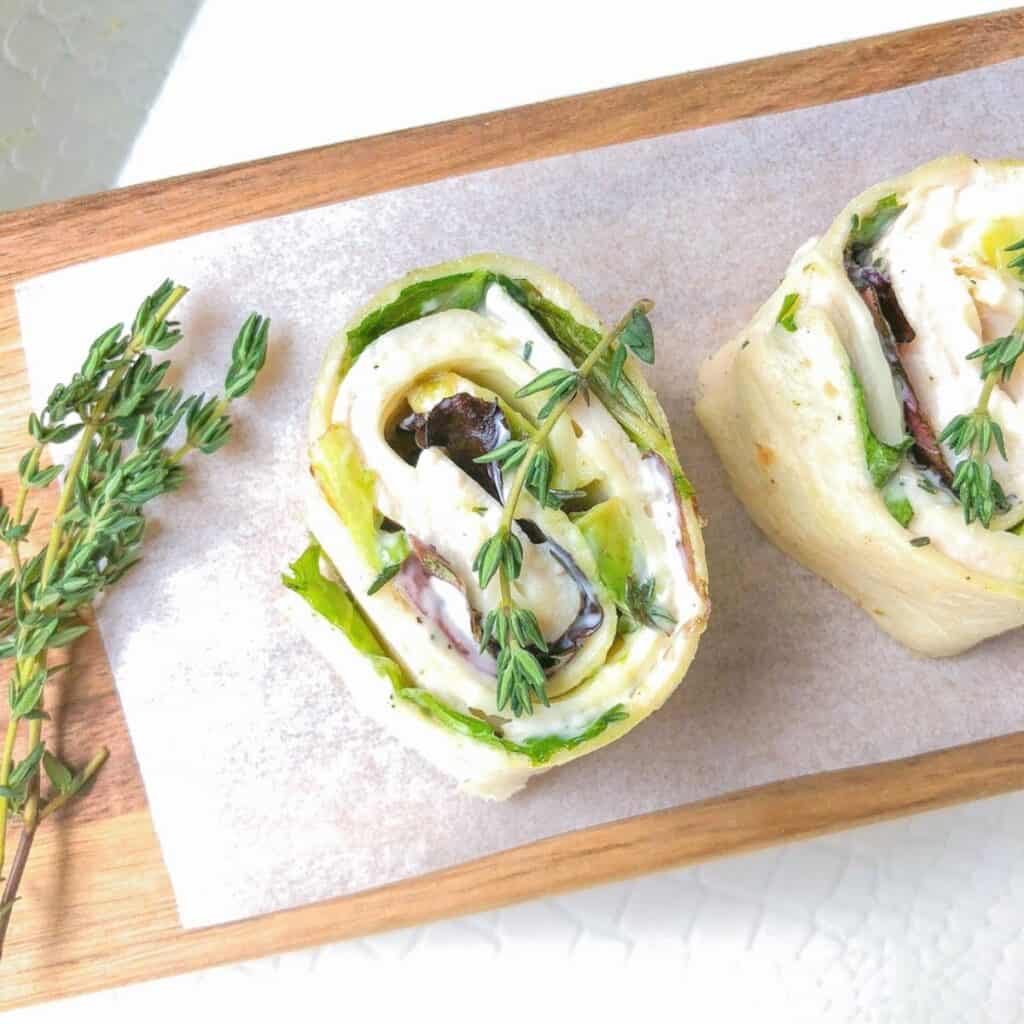 turkey roll ups with cheese, lettuce and dressing laid on a cutting board with fresh tyhme