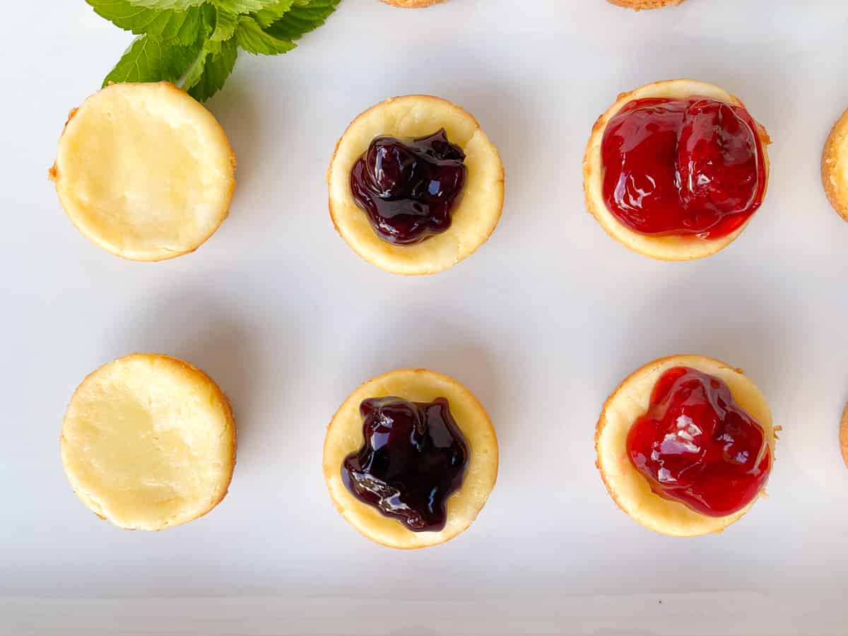 bite-size mini cheesecakes with strawberry and blueberry topping on a white plate.