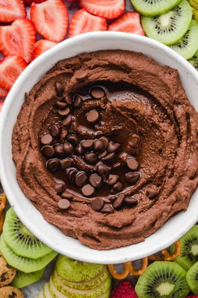 chocolate hummus in a bowl topped with mini chocolate chips and fruit surrounding the bowl.