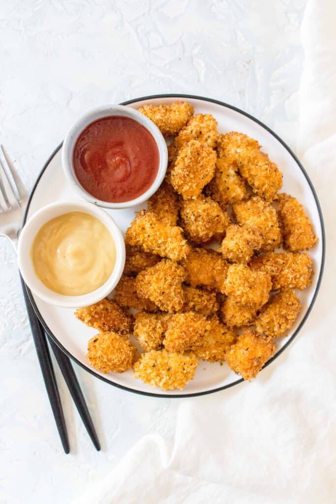 baked chicken nuggets in a bowl with 2 sauces on the side.