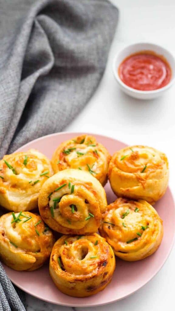 pizza rolls on a pink plate with marinara sauce in the background.
