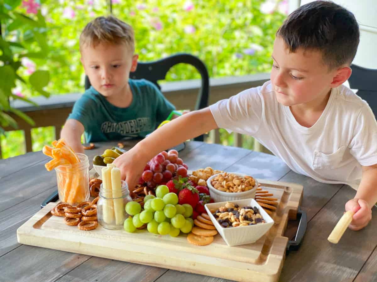 two kids snacking on a large charcuterie board tray