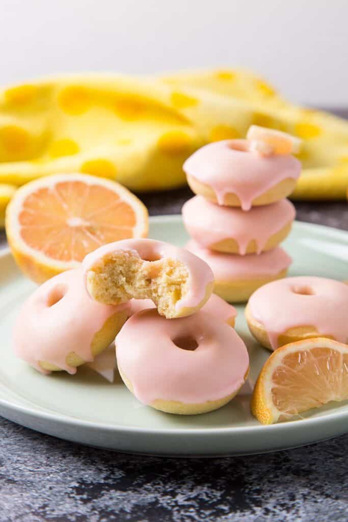 mini donuts on a plate with pink icing and oranges next to them.