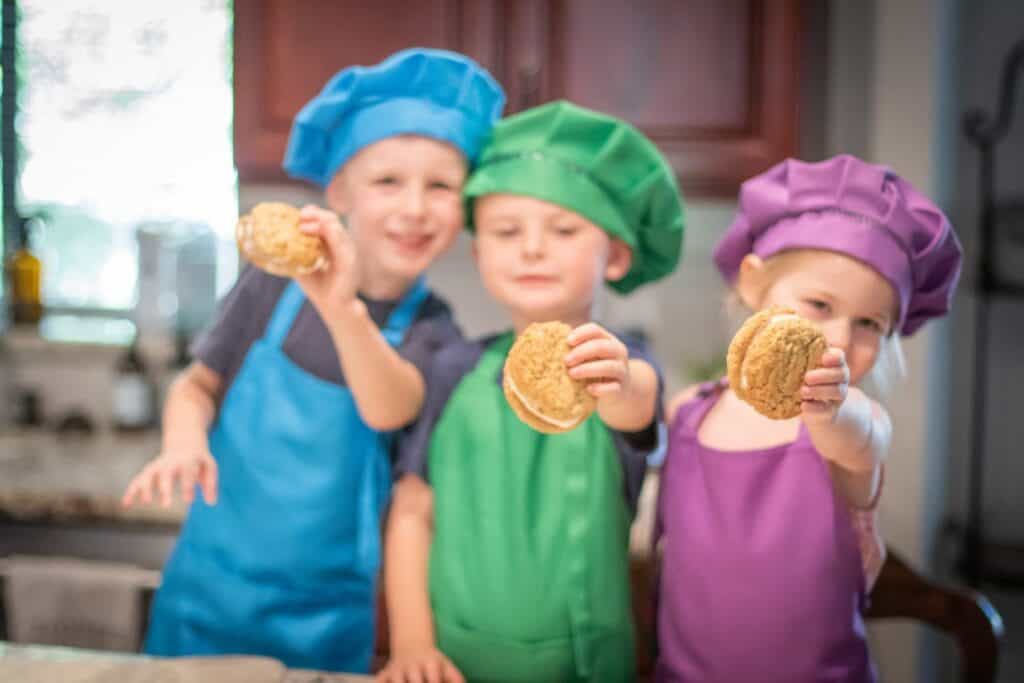 kids wearing aprons and bakers hats holding ice cream sandwiches in their hands.