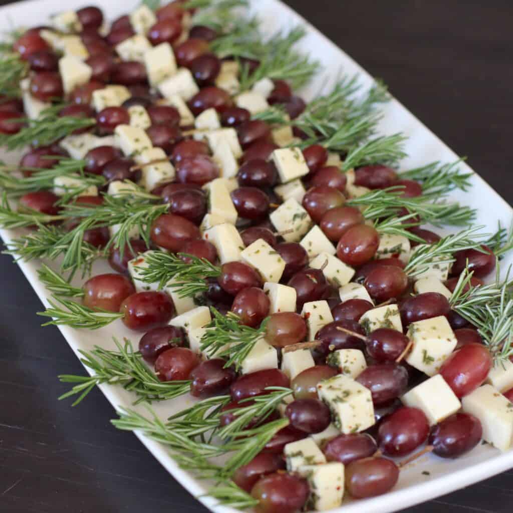grapes and fontina skewered with rosemary on a plate.