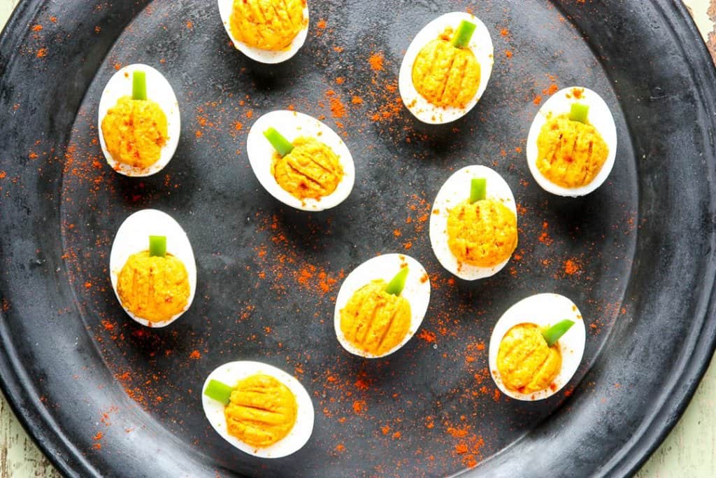 Halloween deviled eggs that look like mini pumpkins appetizer on plate.
