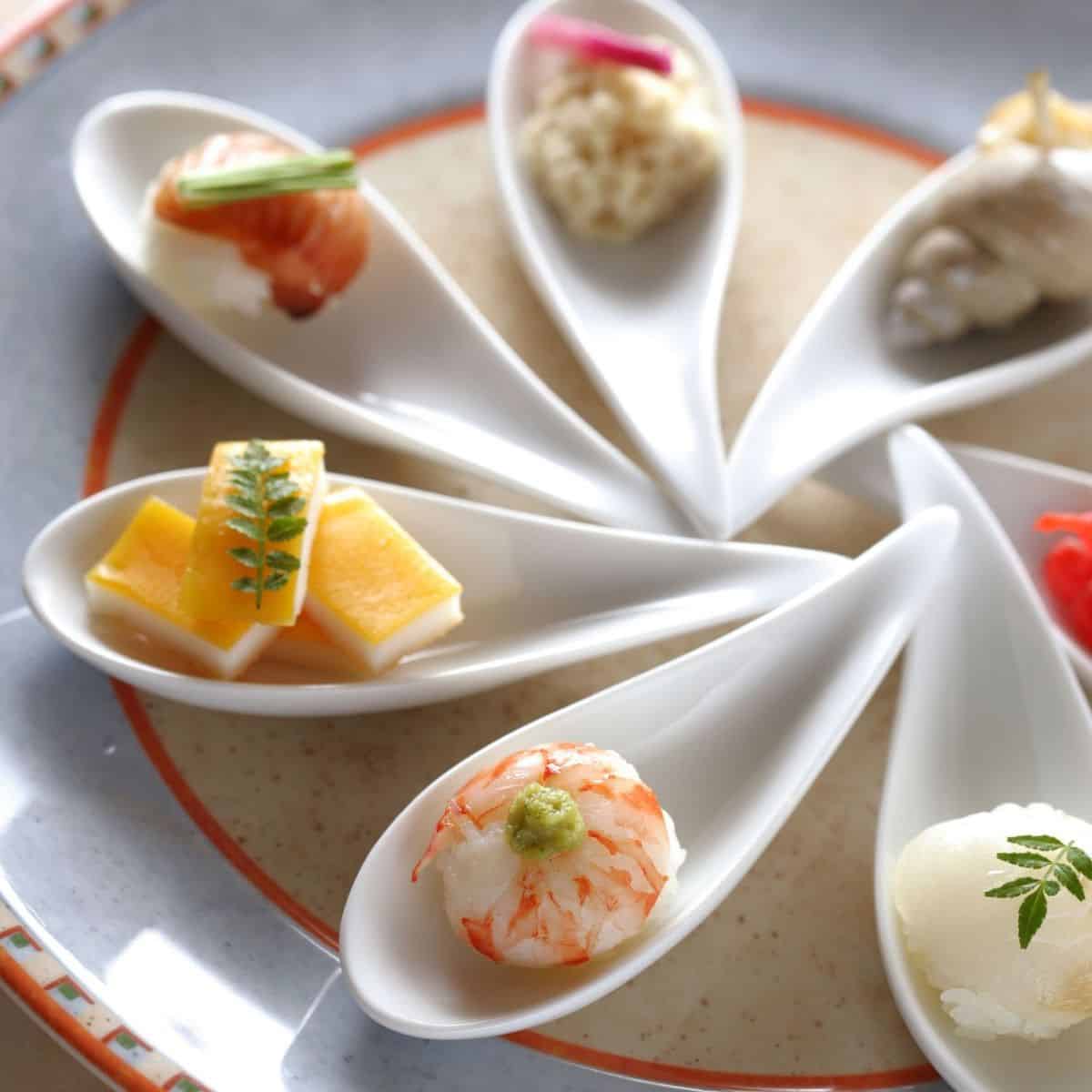 Amuse bouche spoons spread onto a plate with food inside.