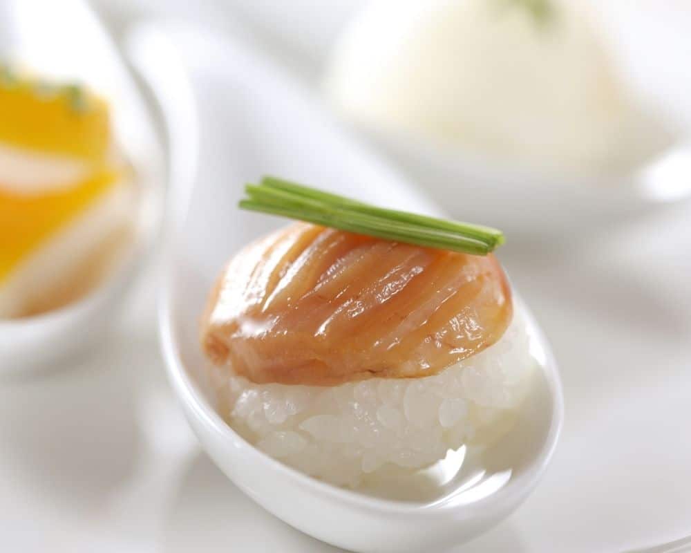 Amuse bouche on a spoon over rice with chive garnish.