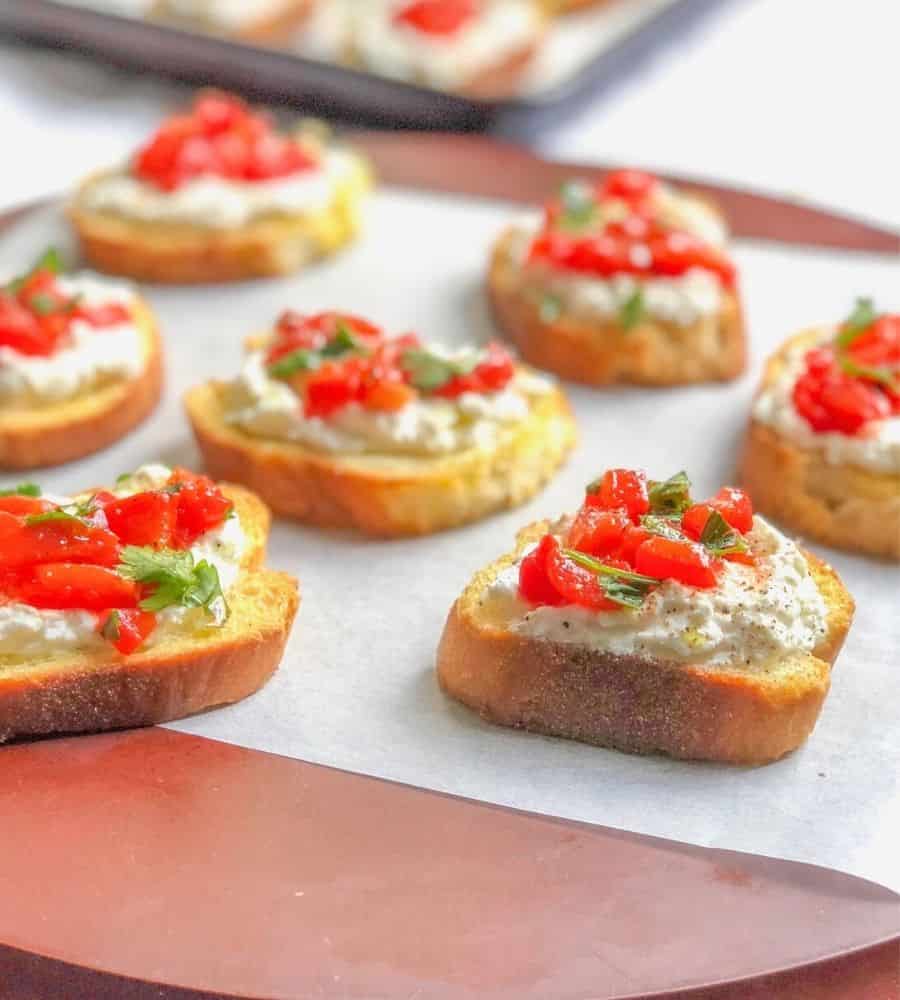 crostini appetizer on a plate topped with ricotta cheese, basil and roasted red peppers