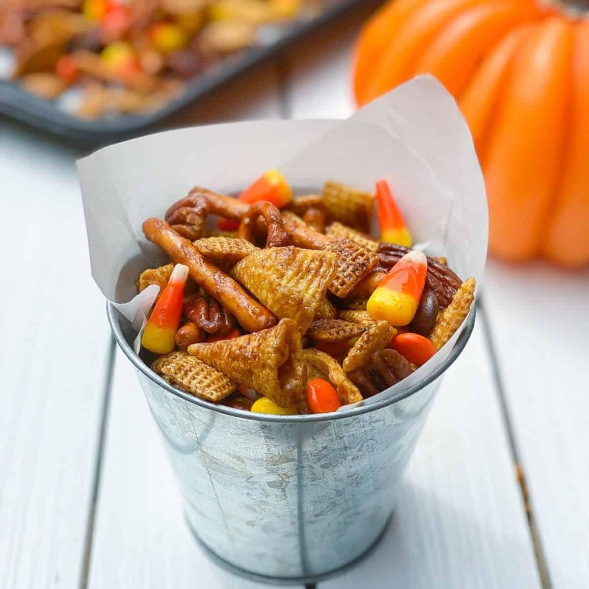 Halloween spiced Chex mix in a metal tin with candy corn.