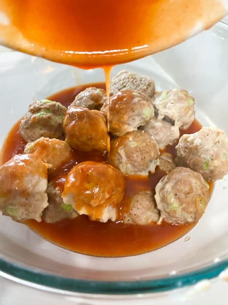 Pouring buffalo sauce ove rmeatballs.