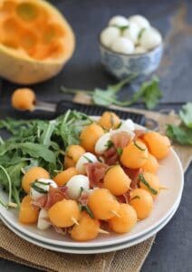 Melon with prosciutto and mozzarella skewers on a plate.