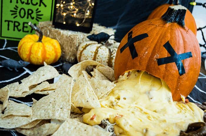large creepy puking pumpkin appetizer with cheese spilling out of the mouth onto nachos.