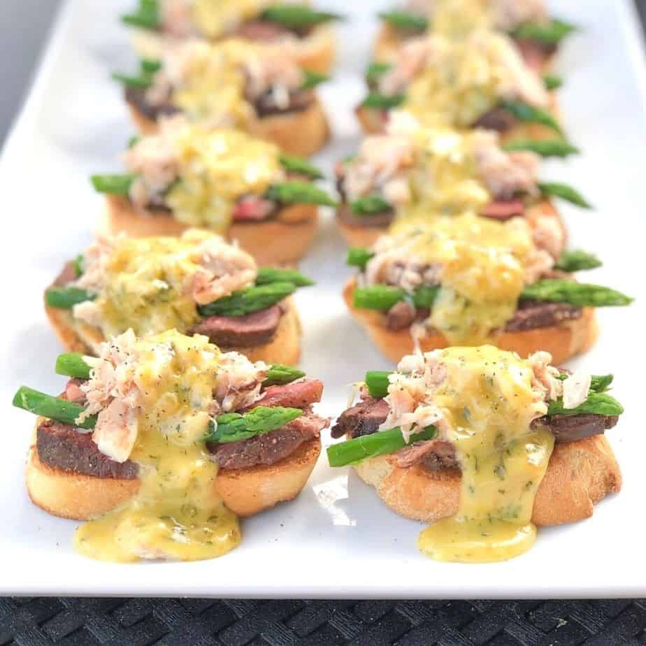 steak and crab over top of crostini with sauce on a platter.